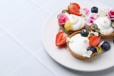 Photo of Delicious dessert. Tartlets with cream, berries and flowers on white tiled table, closeup. Space for text
