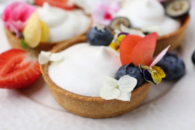 Photo of Delicious dessert. Tartlets with cream, berries and flowers on white tiled table, closeup