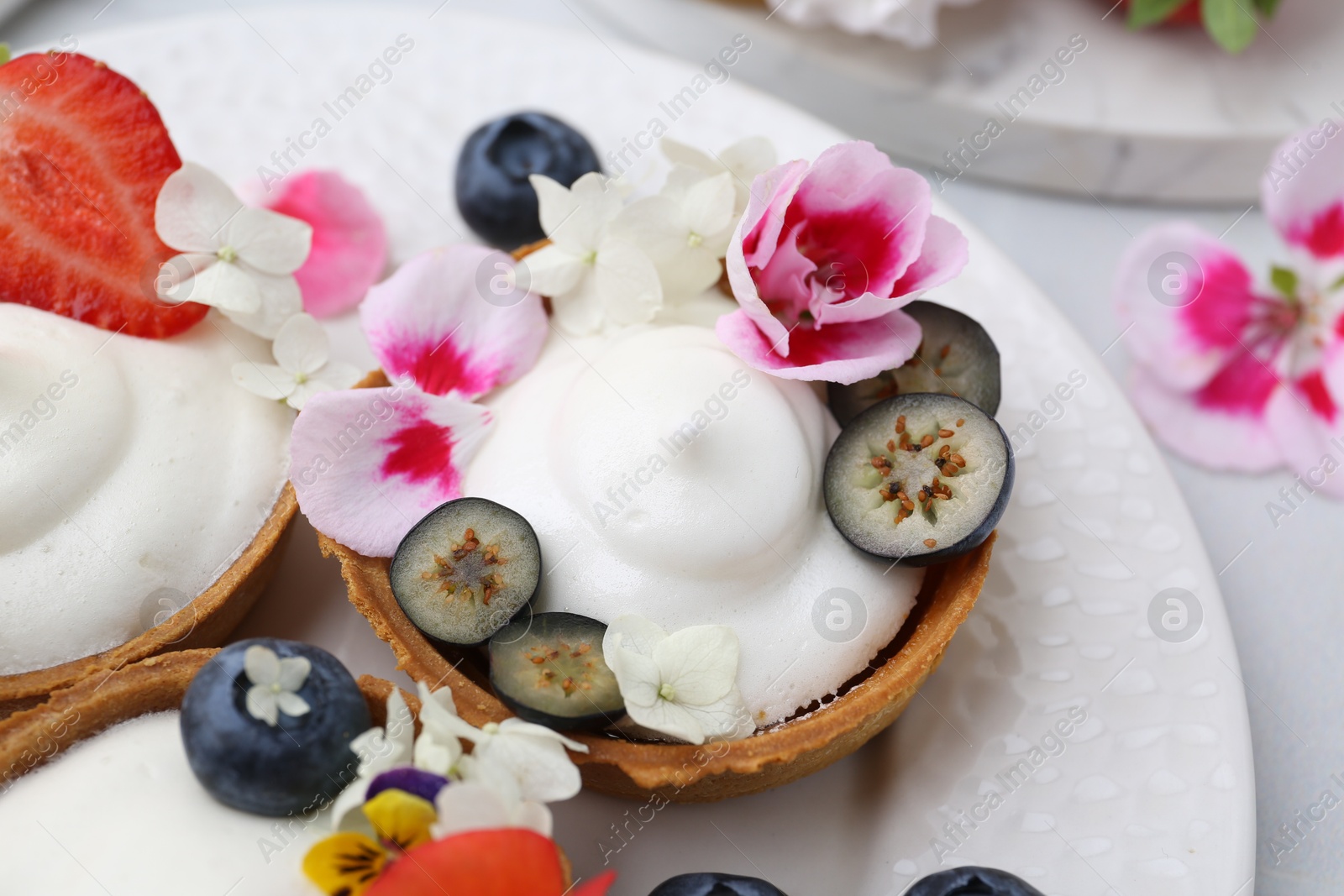 Delicious dessert. Tartlets with cream, berries and flowers on white tiled table, closeup Photo of Delicious dessert. Tartlets with cream, berries and flowers on white tiled table, closeup