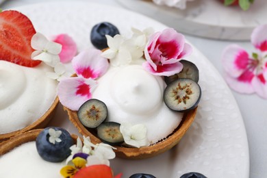Photo of Delicious dessert. Tartlets with cream, berries and flowers on white tiled table, closeup