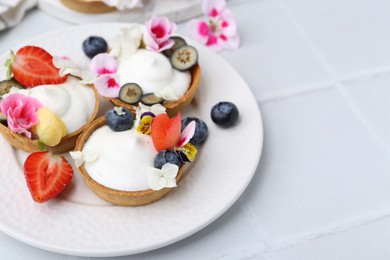 Photo of Delicious dessert. Tartlets with cream, berries and flowers on white tiled table, closeup. Space for text