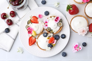 Photo of Delicious dessert. Tartlets with cream, berries and flowers on white tiled table, flat lay