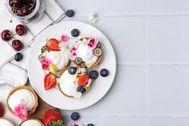 Photo of Delicious dessert. Tartlets with cream, berries and flowers on white tiled table, flat lay. Space for text
