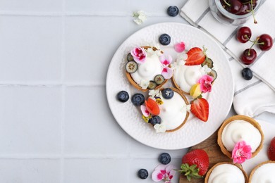 Photo of Delicious dessert. Tartlets with cream, berries and flowers on white tiled table, flat lay. Space for text