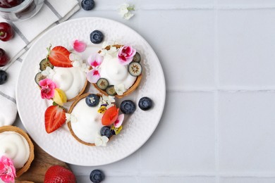 Photo of Delicious dessert. Tartlets with cream, berries and flowers on white tiled table, flat lay. Space for text