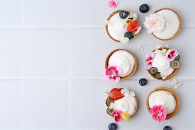 Photo of Delicious dessert. Tartlets with cream, berries and flowers on white tiled table, flat lay. Space for text