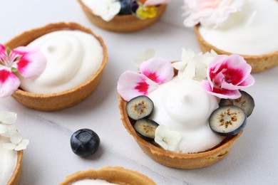 Photo of Delicious dessert. Tartlets with cream, berries and flowers on white tiled table, closeup