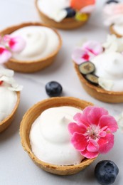 Photo of Delicious dessert. Tartlets with cream, berries and flowers on white tiled table, closeup