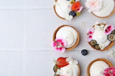 Photo of Delicious dessert. Tartlets with cream, berries and flowers on white tiled table, flat lay. Space for text
