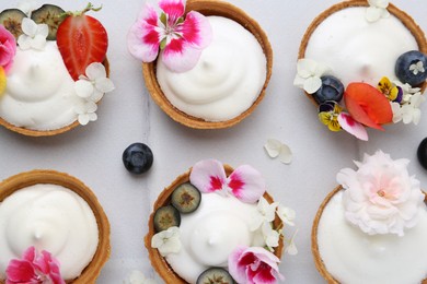 Photo of Delicious dessert. Tartlets with cream, berries and flowers on white tiled table, flat lay