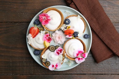 Photo of Delicious dessert. Tartlets with cream, berries and flowers on wooden table, top view