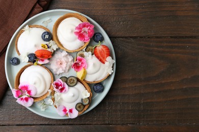 Photo of Delicious dessert. Tartlets with cream, berries and flowers on wooden table, top view. Space for text