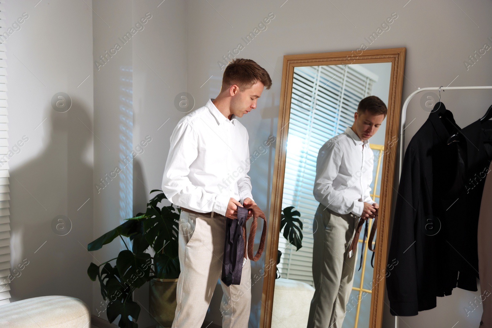 Handsome man choosing neckties while getting ready near mirror indoors Photo of Handsome man choosing neckties while getting ready near mirror indoors