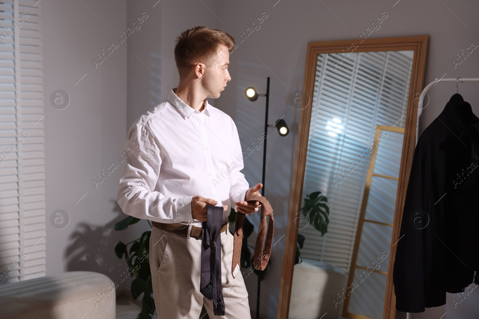 Handsome man choosing neckties while getting ready near mirror indoors Photo of Handsome man choosing neckties while getting ready near mirror indoors