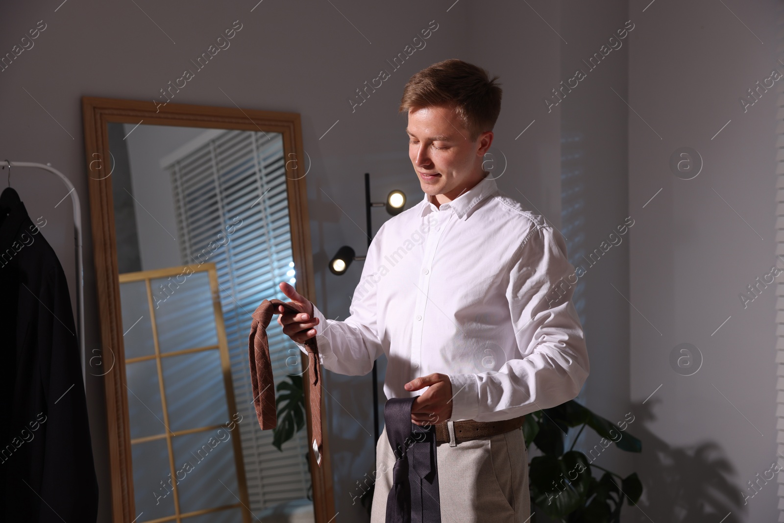 Handsome man choosing neckties while getting ready near mirror indoors Photo of Handsome man choosing neckties while getting ready near mirror indoors