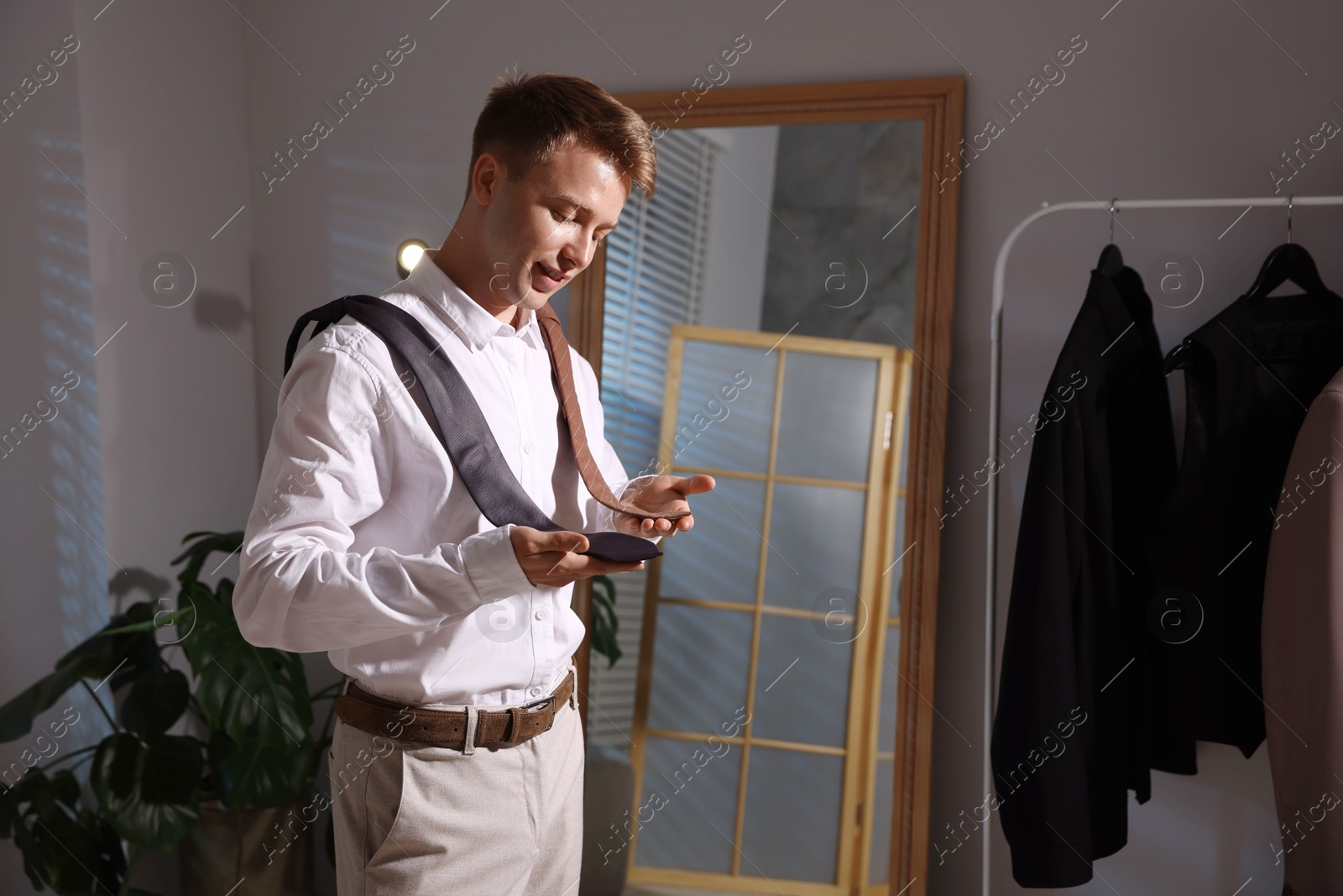 Handsome man choosing neckties while getting ready near mirror indoors Photo of Handsome man choosing neckties while getting ready near mirror indoors