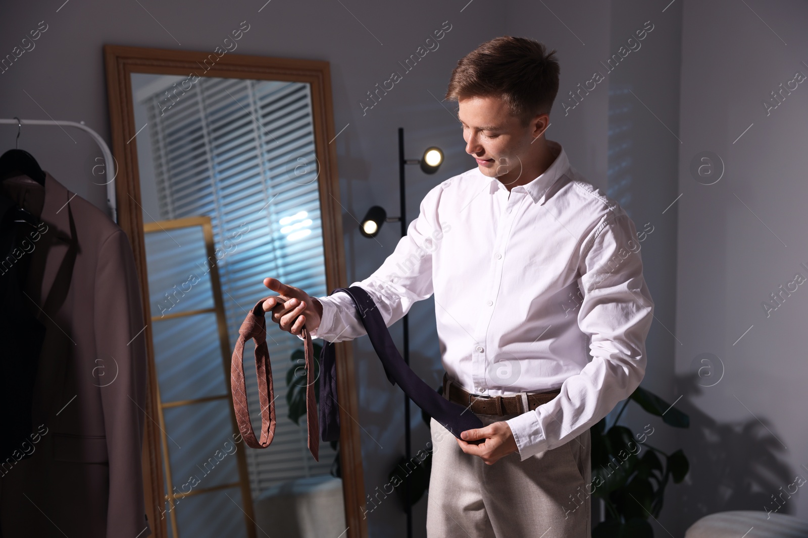 Handsome man choosing neckties while getting ready near mirror indoors Photo of Handsome man choosing neckties while getting ready near mirror indoors