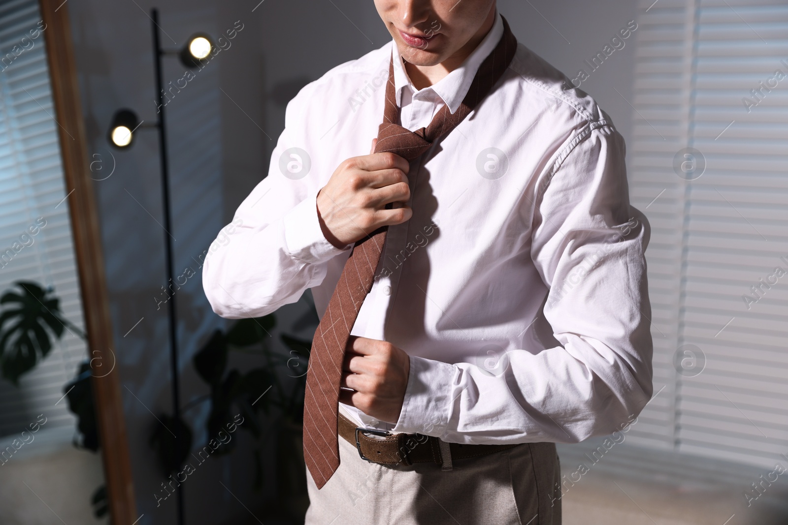Man adjusting necktie while getting ready indoors, closeup Photo of Man adjusting necktie while getting ready indoors, closeup