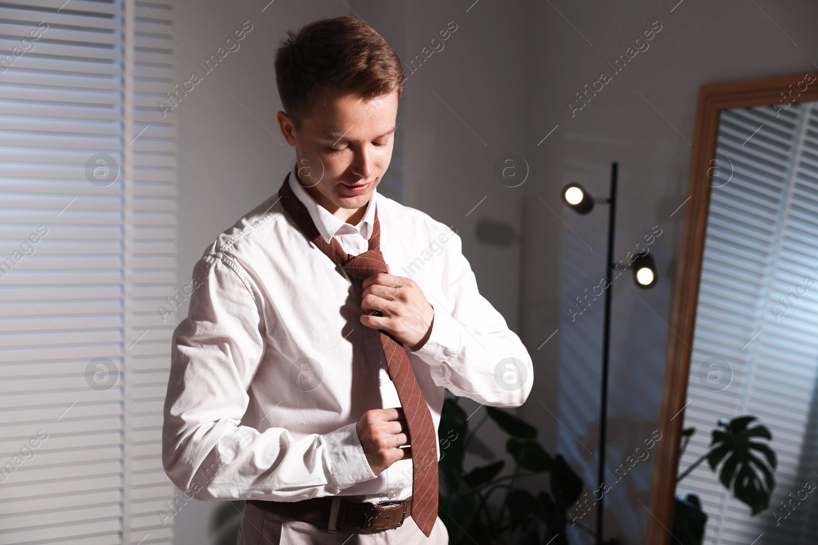 Man adjusting necktie while getting ready indoors Photo of Man adjusting necktie while getting ready indoors