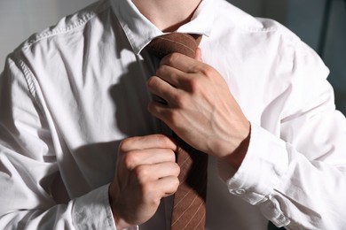 Photo of Man adjusting necktie while getting ready indoors, closeup