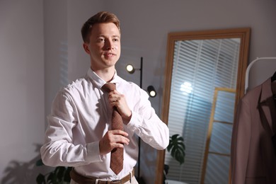 Photo of Man adjusting necktie while getting ready indoors, space for text