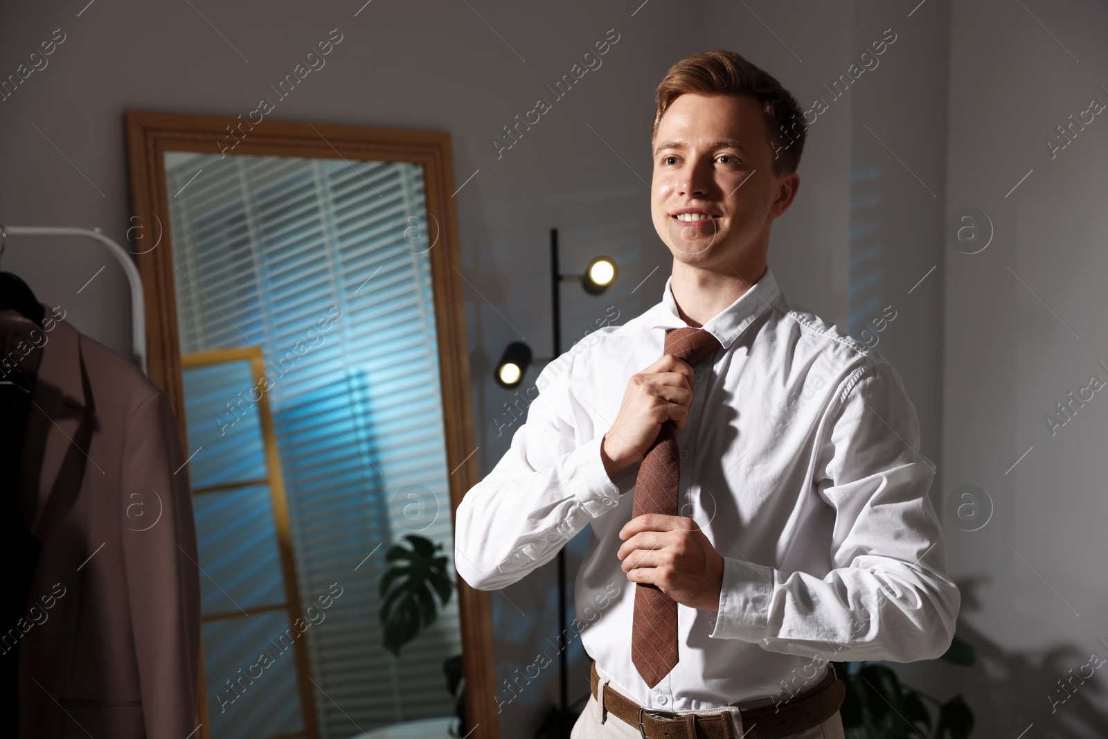 Man adjusting necktie while getting ready indoors, space for text Photo of Man adjusting necktie while getting ready indoors, space for text