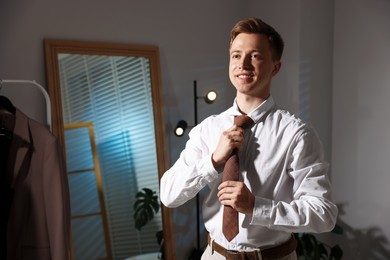 Photo of Man adjusting necktie while getting ready indoors, space for text