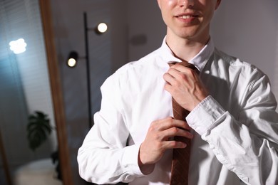 Photo of Man adjusting necktie while getting ready indoors, closeup