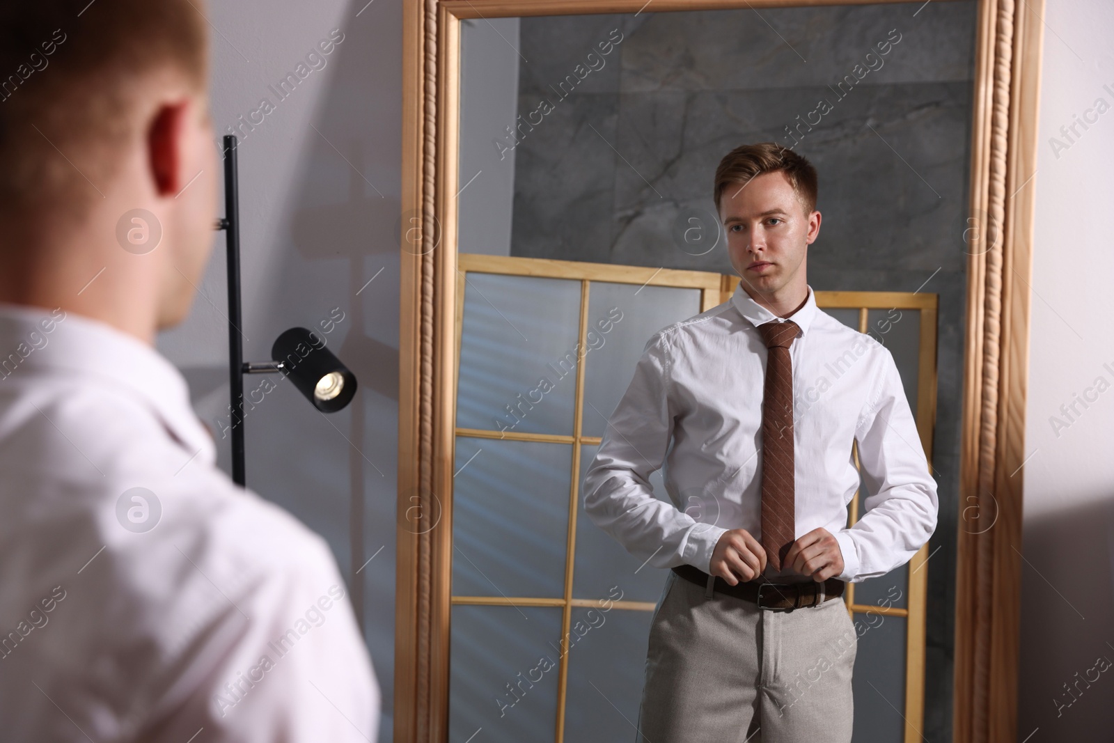 Handsome man getting ready near mirror indoors Photo of Handsome man getting ready near mirror indoors