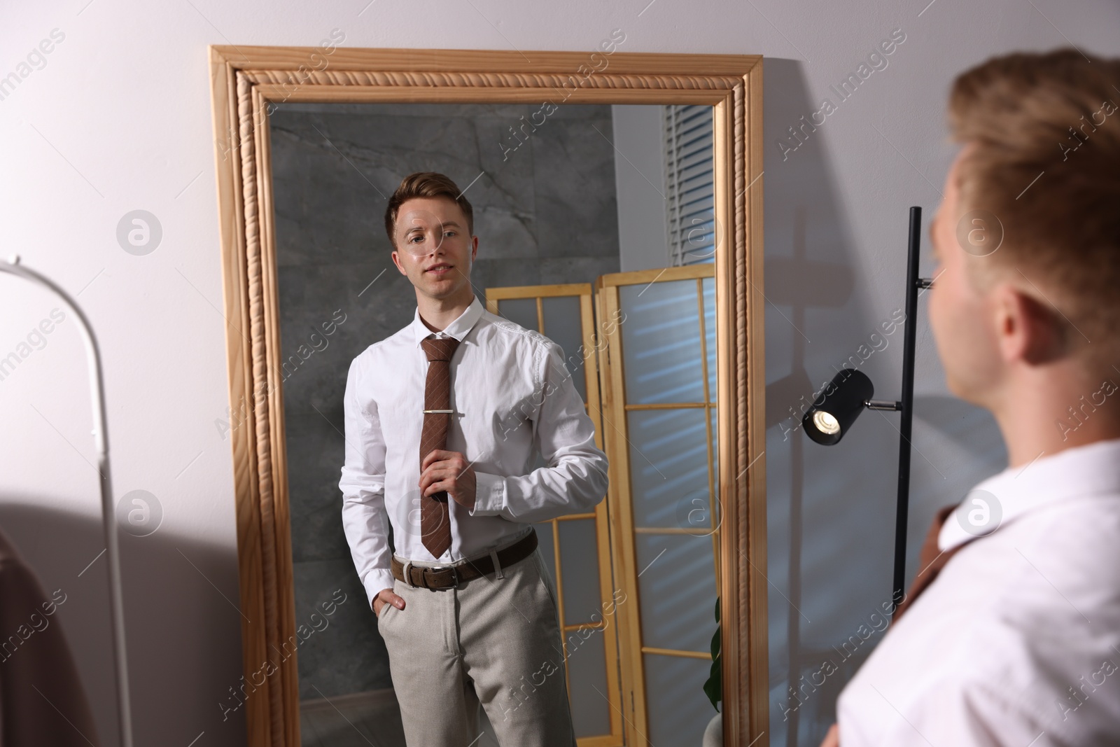 Handsome man getting ready near mirror indoors Photo of Handsome man getting ready near mirror indoors