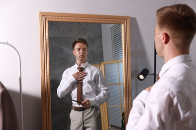 Photo of Handsome man brushing his hair while getting ready near mirror indoors