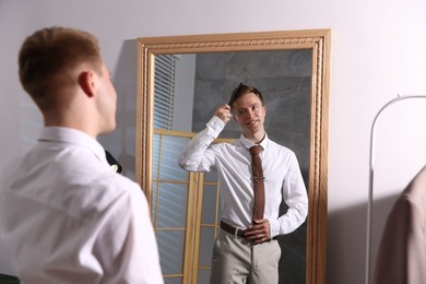 Photo of Handsome man brushing his hair while getting ready near mirror indoors