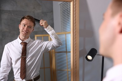 Photo of Handsome man brushing his hair while getting ready near mirror indoors