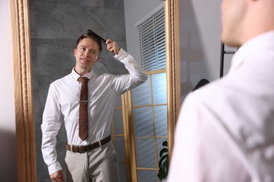 Photo of Handsome man brushing his hair while getting ready near mirror indoors