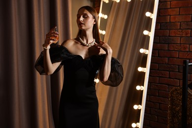Photo of Woman spraying perfume while getting ready near mirror indoors