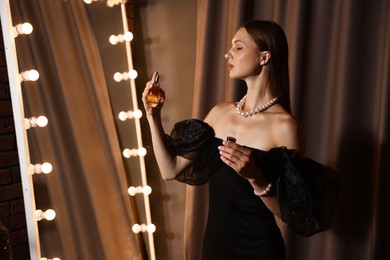 Photo of Woman spraying perfume while getting ready near mirror indoors