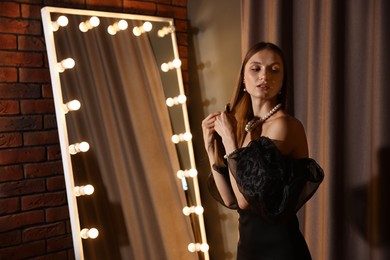 Photo of Beautiful woman brushing her hair while getting ready near mirror indoors