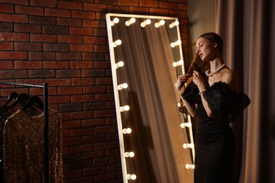 Photo of Beautiful woman brushing her hair while getting ready near mirror indoors