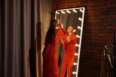 Photo of Beautiful woman applying mascara while getting ready near mirror indoors