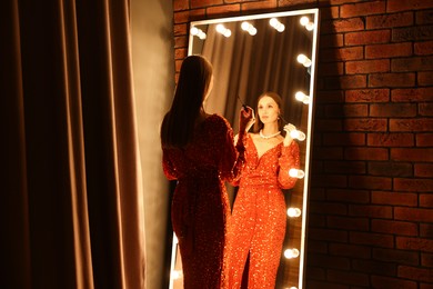 Photo of Beautiful woman applying mascara while getting ready near mirror indoors