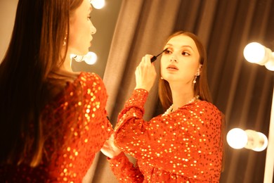 Photo of Beautiful woman applying mascara while getting ready near mirror indoors