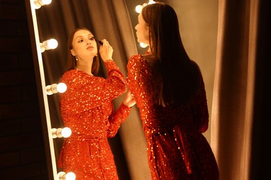 Photo of Beautiful woman applying mascara while getting ready near mirror indoors