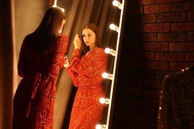 Photo of Beautiful woman applying mascara while getting ready near mirror indoors