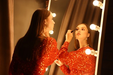 Photo of Beautiful woman applying mascara while getting ready near mirror indoors