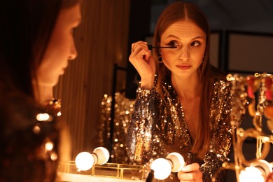 Photo of Beautiful woman applying mascara while getting ready at dressing table indoors