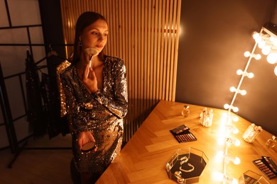 Photo of Beautiful woman applying makeup while getting ready at dressing table indoors