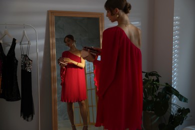 Photo of Beautiful woman with stylish bag getting ready near mirror indoors