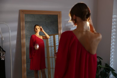 Photo of Beautiful woman with stylish bag getting ready near mirror indoors