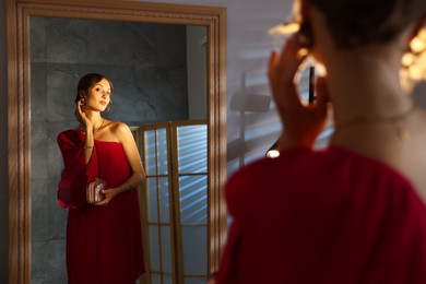 Photo of Beautiful woman with stylish bag getting ready near mirror indoors