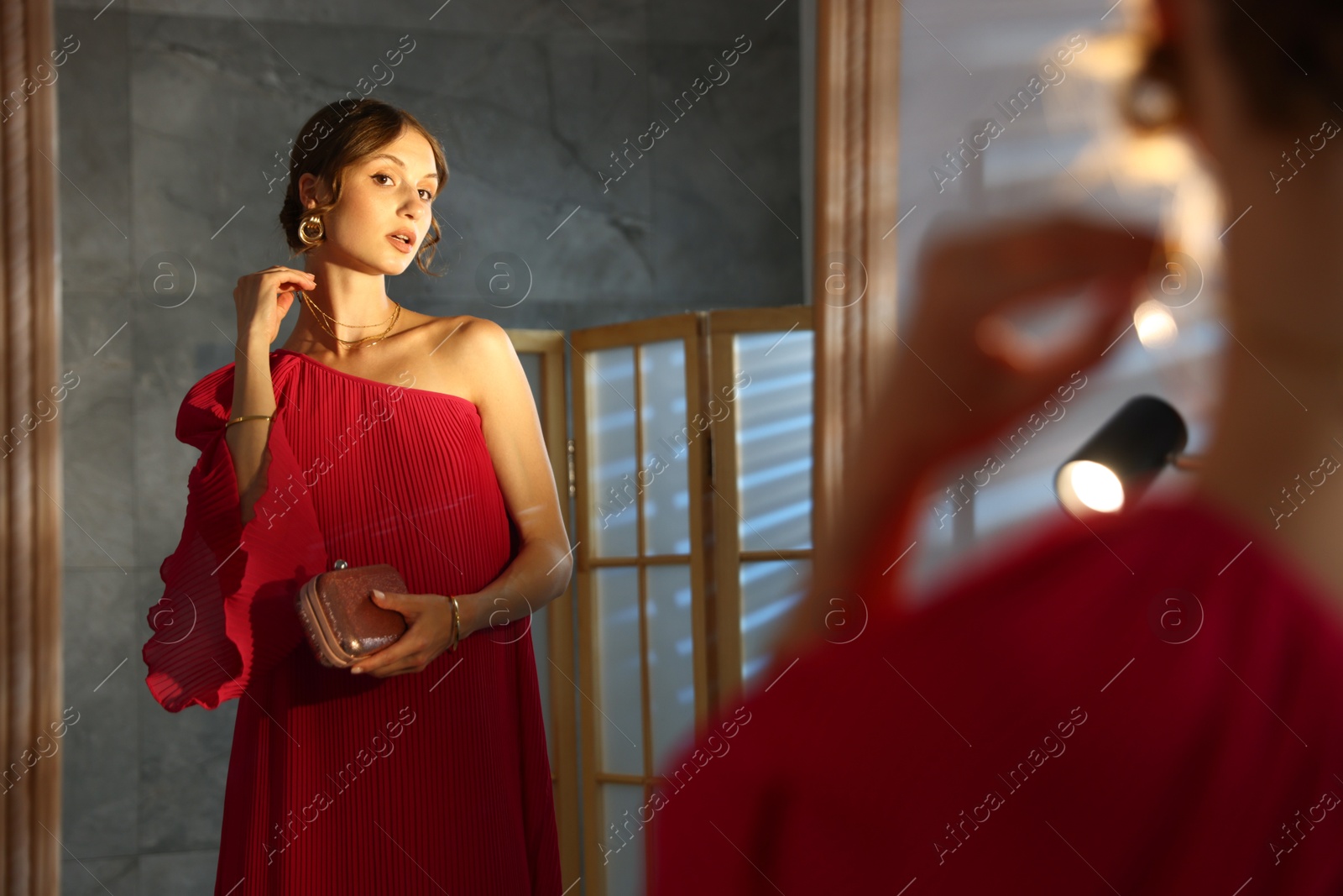 Beautiful woman with stylish bag getting ready near mirror indoors Photo of Beautiful woman with stylish bag getting ready near mirror indoors